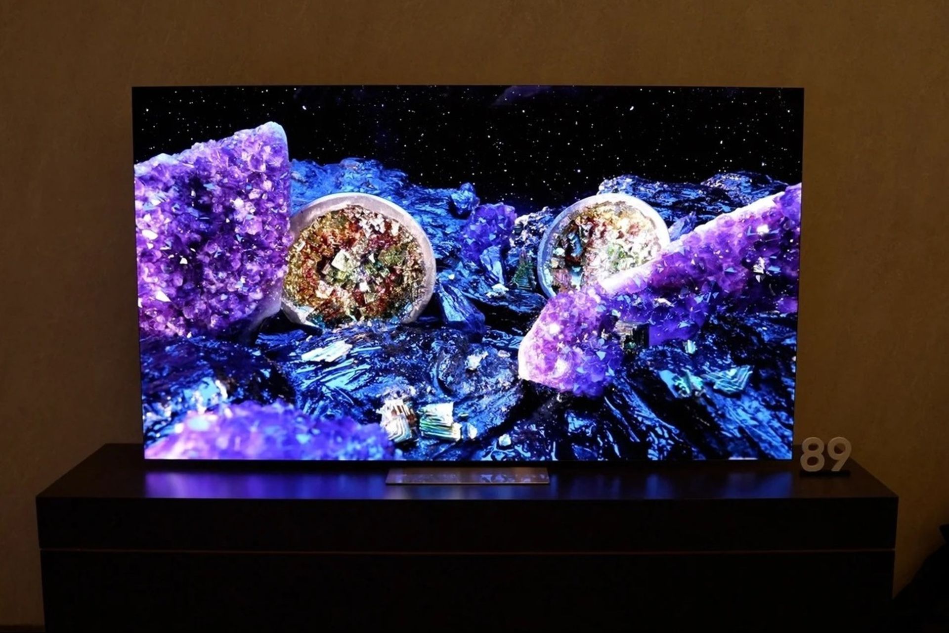 نمای روبرو از تلوزیون QLED 4K QE1C سامسونگ که روی میز تلوزیون چوبی قرار گرفته است