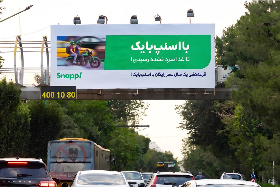 بیلبورد تبلیغاتی اسنپ‌بایک (Snapp!) در کنار جاده با تصویر موتورسوار
