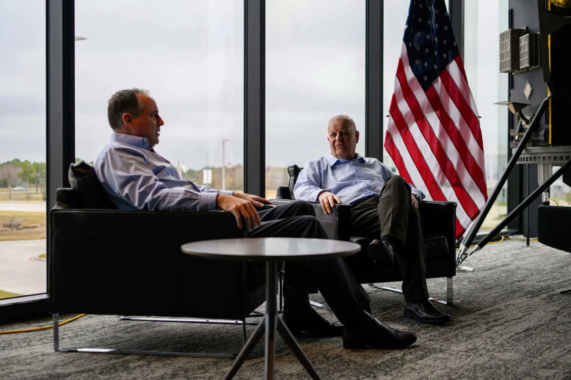استیون آلتموس و کمال غفاریان درمقابل پنجره و در کنار پرچم آمریکا نشسته‌اند