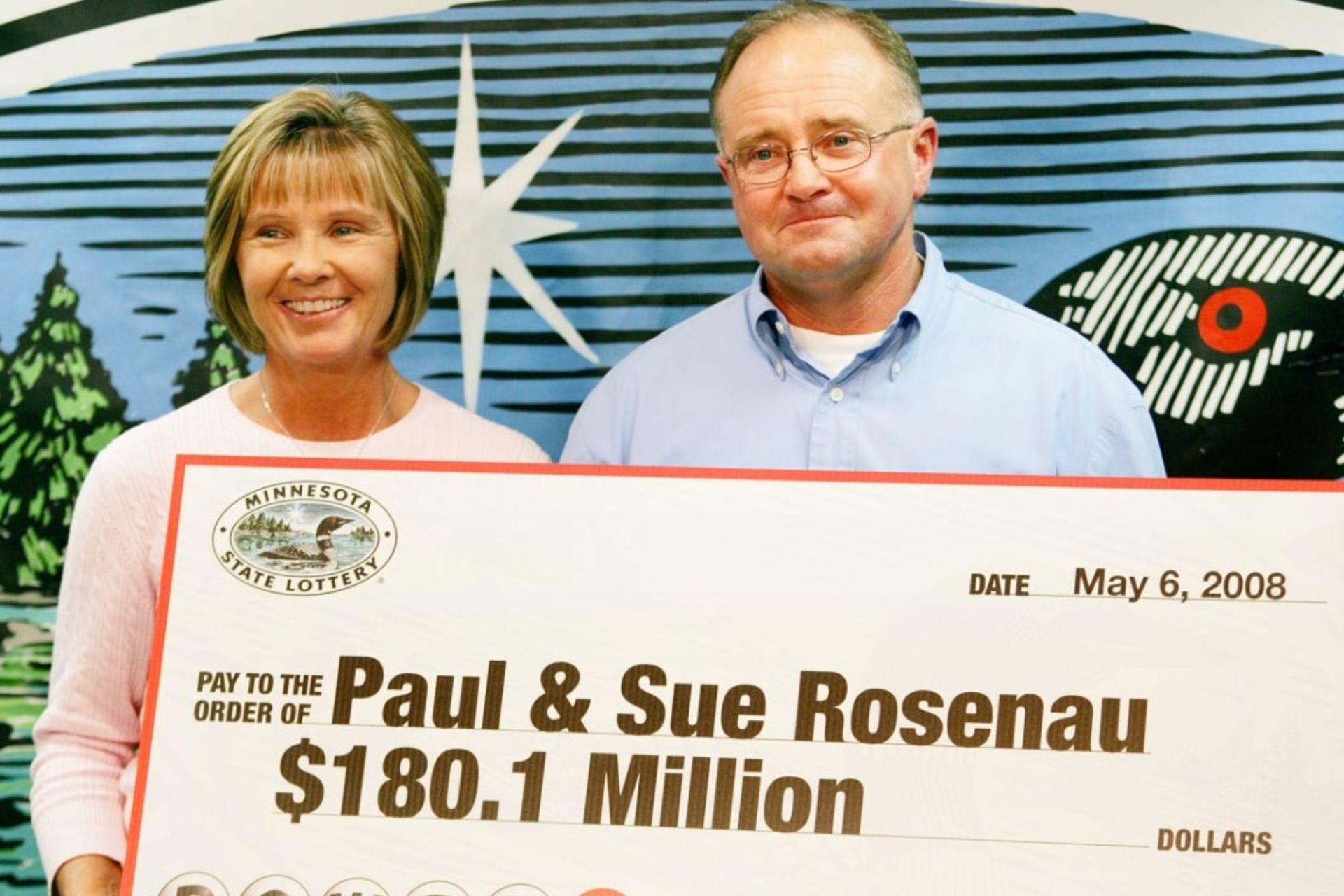 یک مرد و زن میان‌سال با تابلو پیروزی در قرعه‌کشی در دست