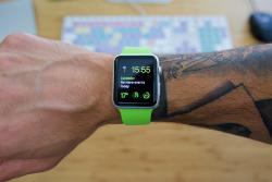 ساعت هوشمندی با بند سبز رپی دست فردی که تتو دارد دیده می شود