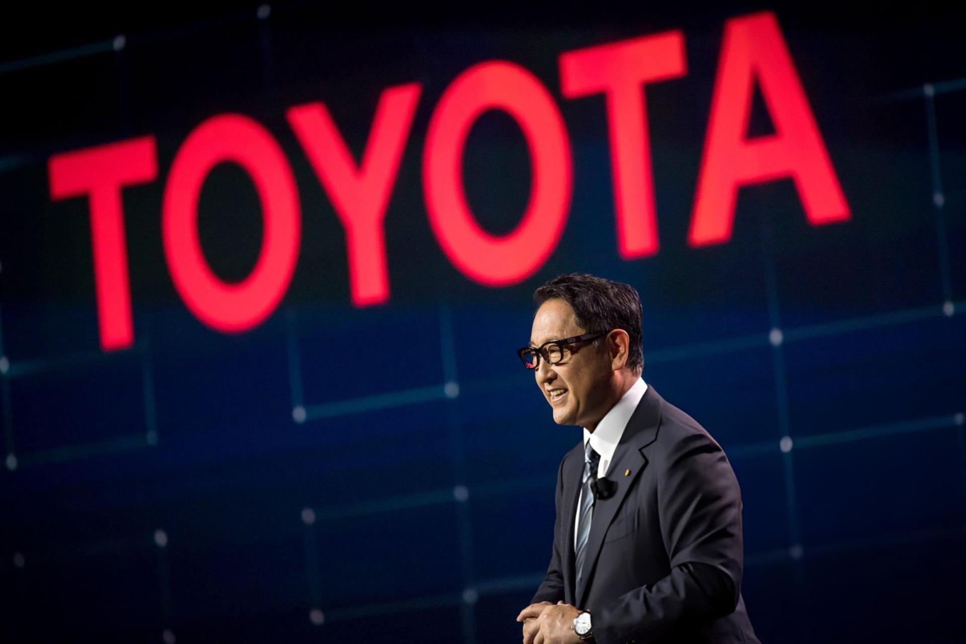 مدیرعامل تویوتا (Toyota) در مقابل لوگوی بزرگ قرمز رنگ این شرکت