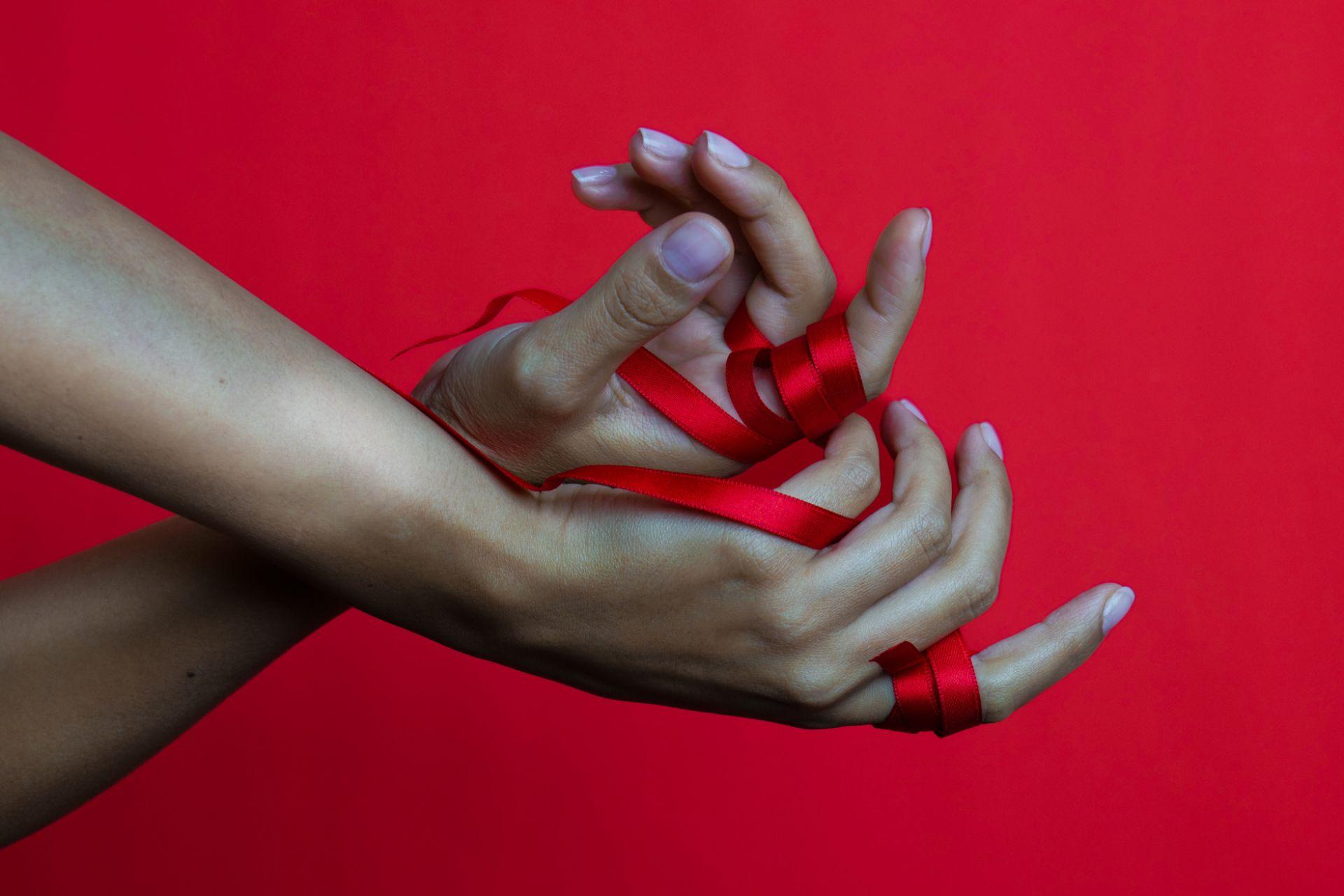 نمای نزدیک از دو دست در پس‌زمینه‌ای قرمز با روبان قرمز به نشانه پیوند عمیق و مفهوم علمی جفت روحی.