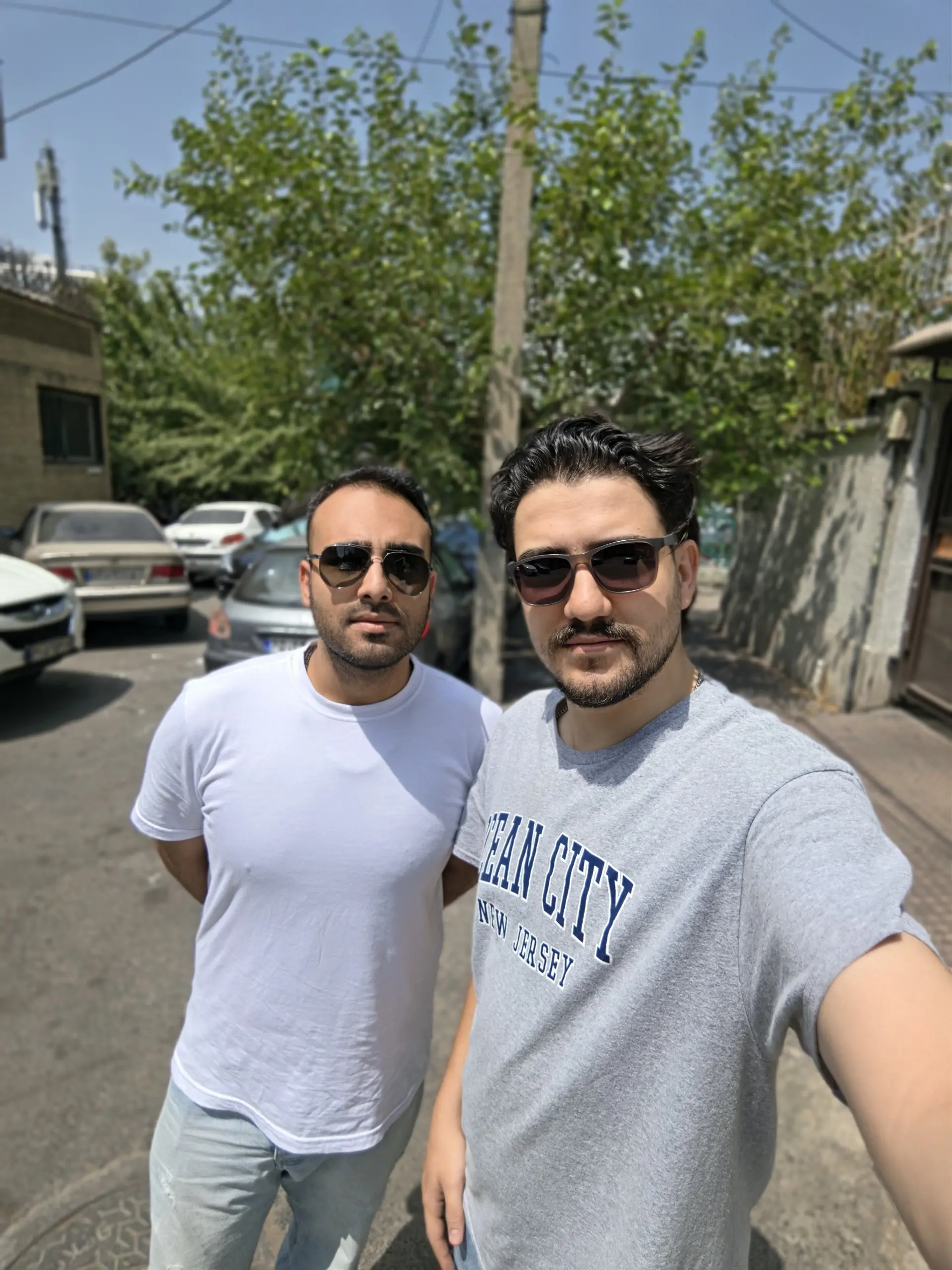 دو مرد با عینک آفتابی در یک خیابان شهری ایستادهاند
