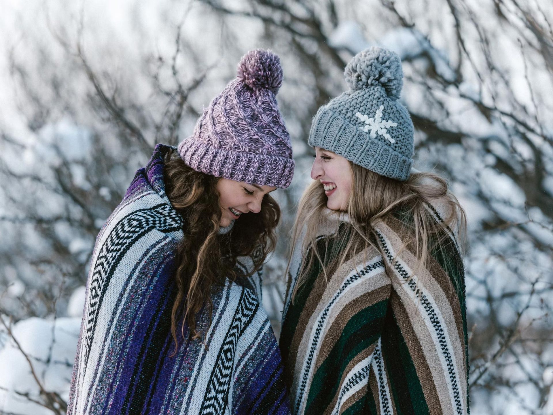 دو زن جوان و خندان پتوپیچ و کلاه به سر در فضای باز زمستانی و برفی