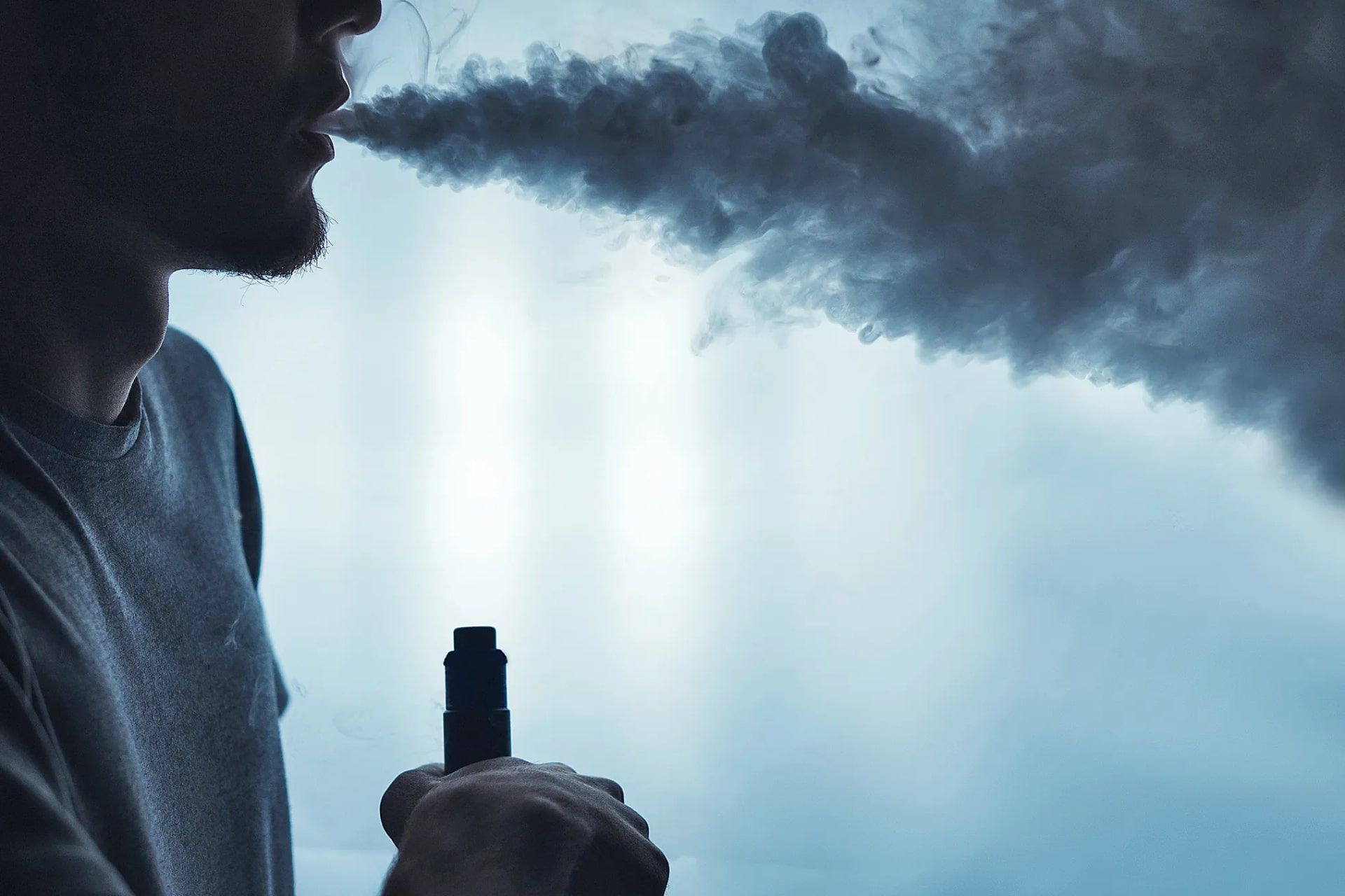 مرد جوان در حال استعمال سیگار الکترونیکی زمینه آبی