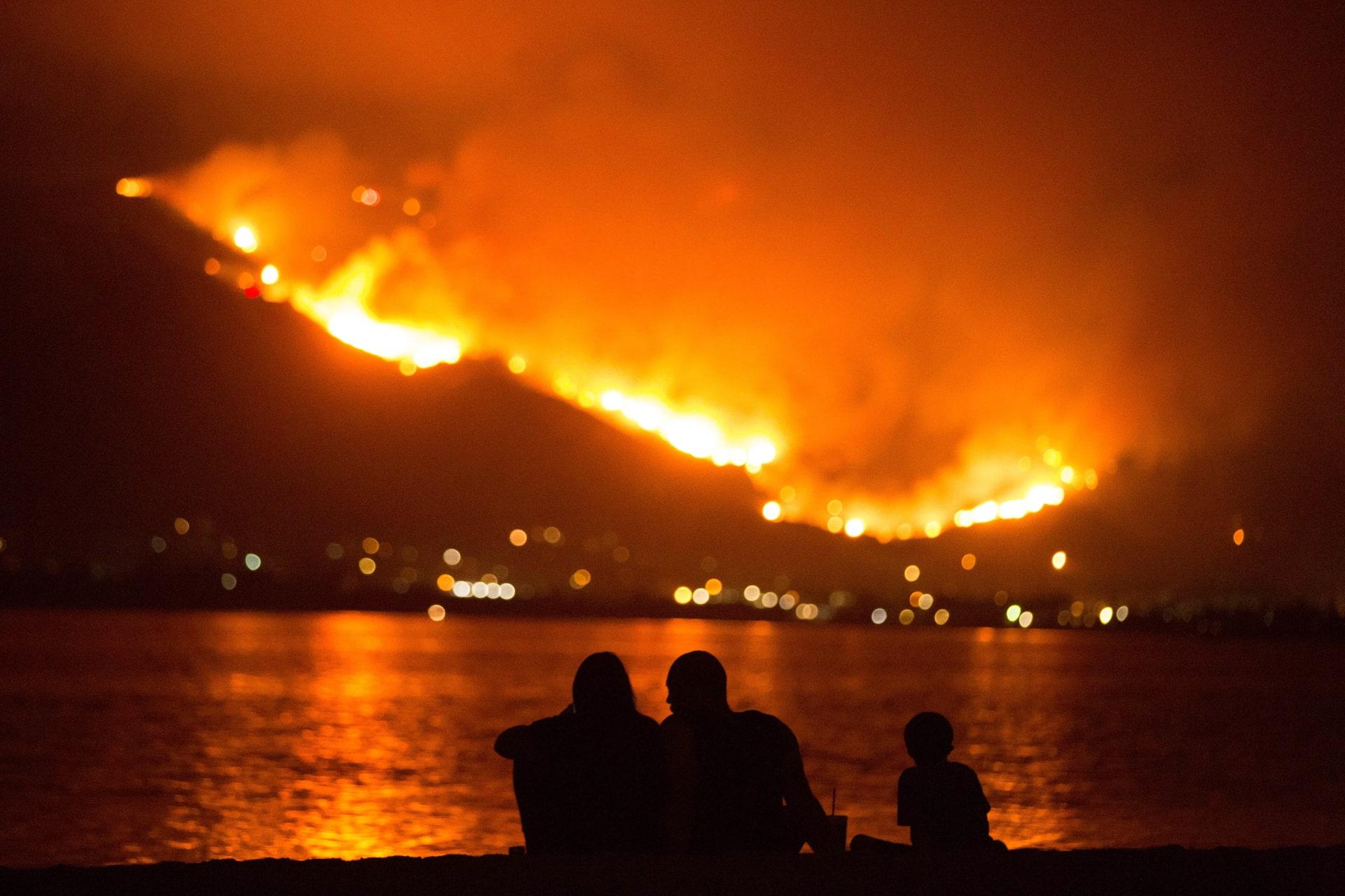 خانواده‌ای در کالیفرنیا کنار ساحل دریاچه السینور نشسته‌اند و آتش‌سوزی را تماشا می کنند.