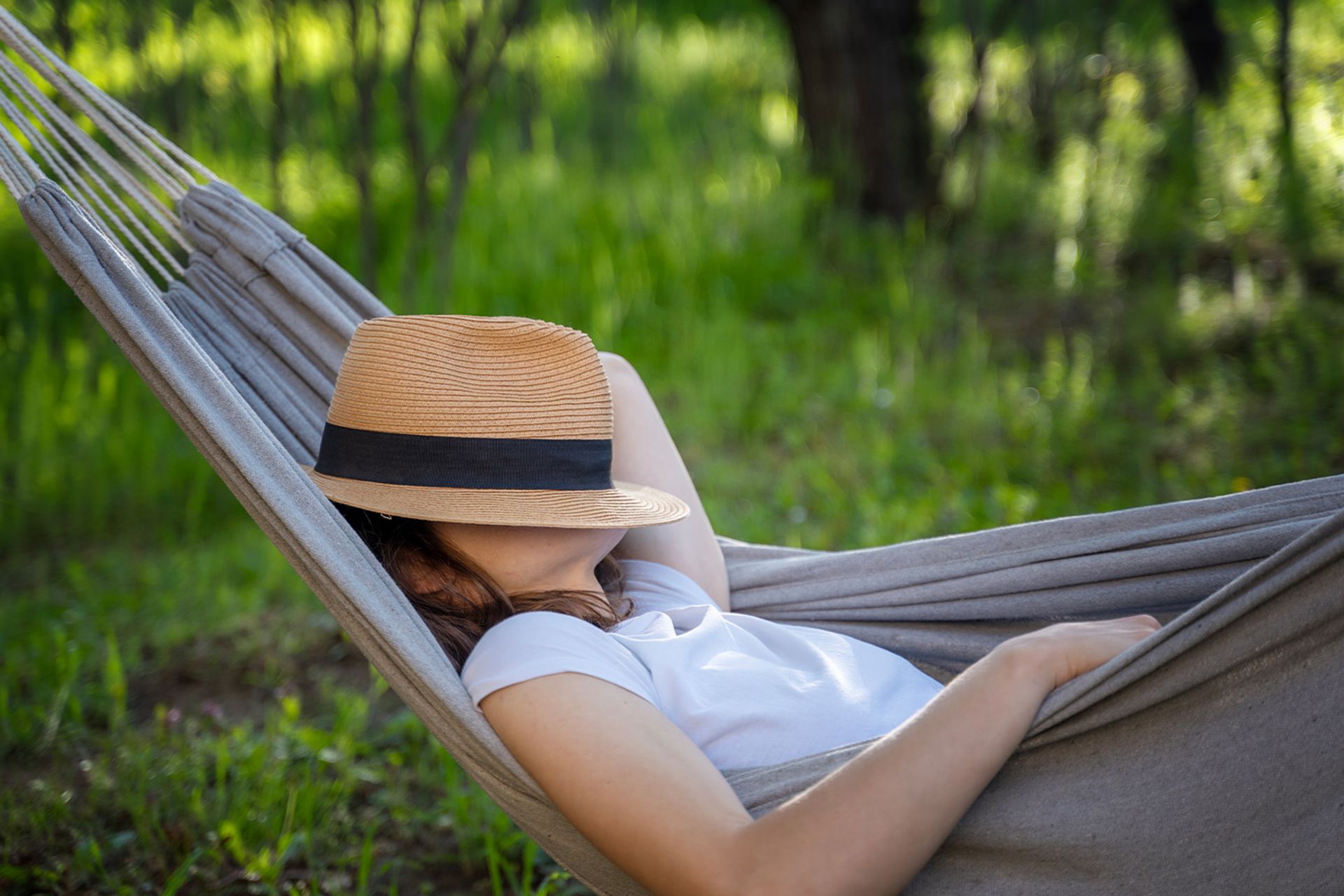 خانمی در یک باغ، روی یک ننو استراحت می‌کند و صورتش را با یک کلاه حصیری پوشانده است