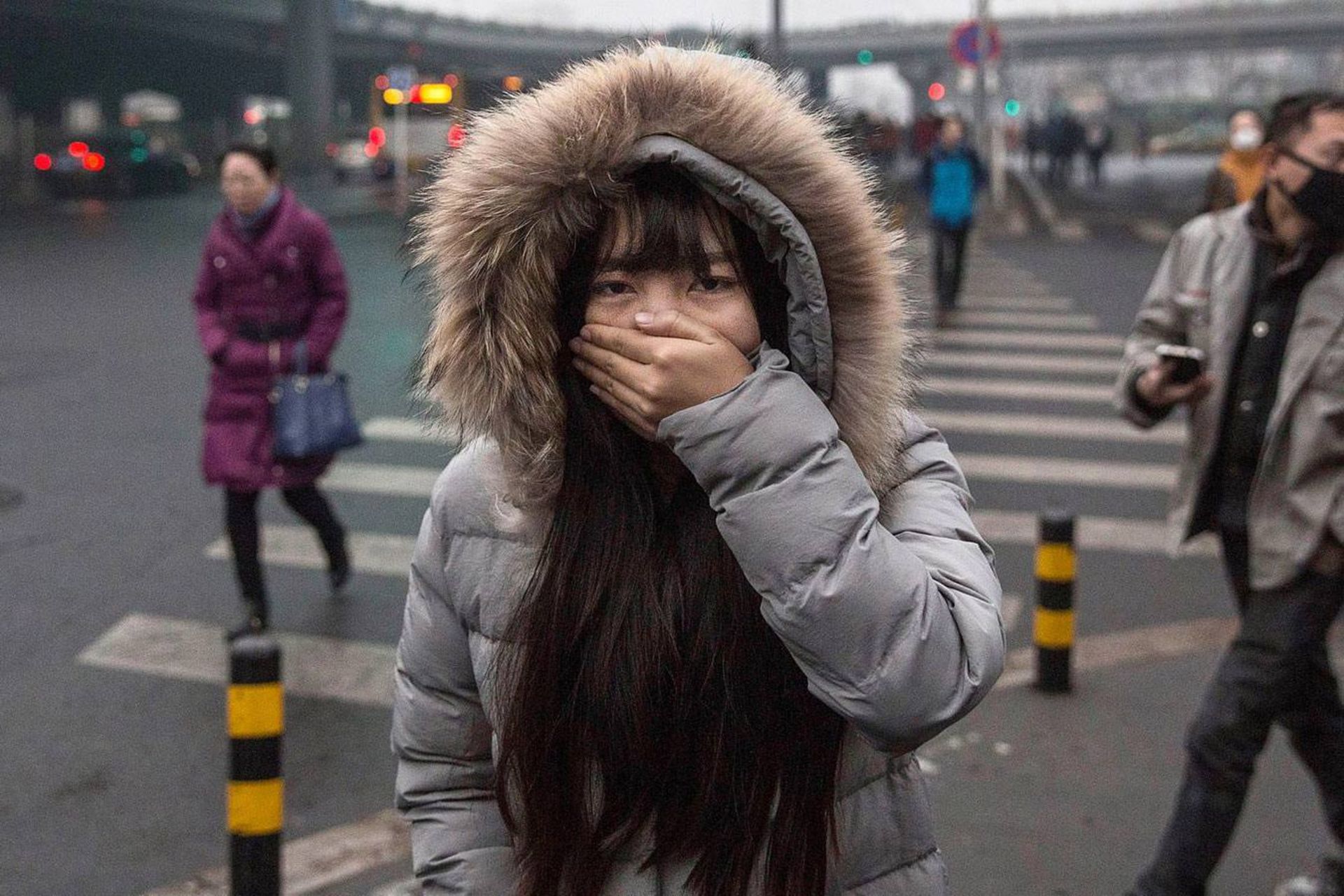 زن جوان رو به دوربین در خیابان ایستاده و دهانش را با دست گرفته است