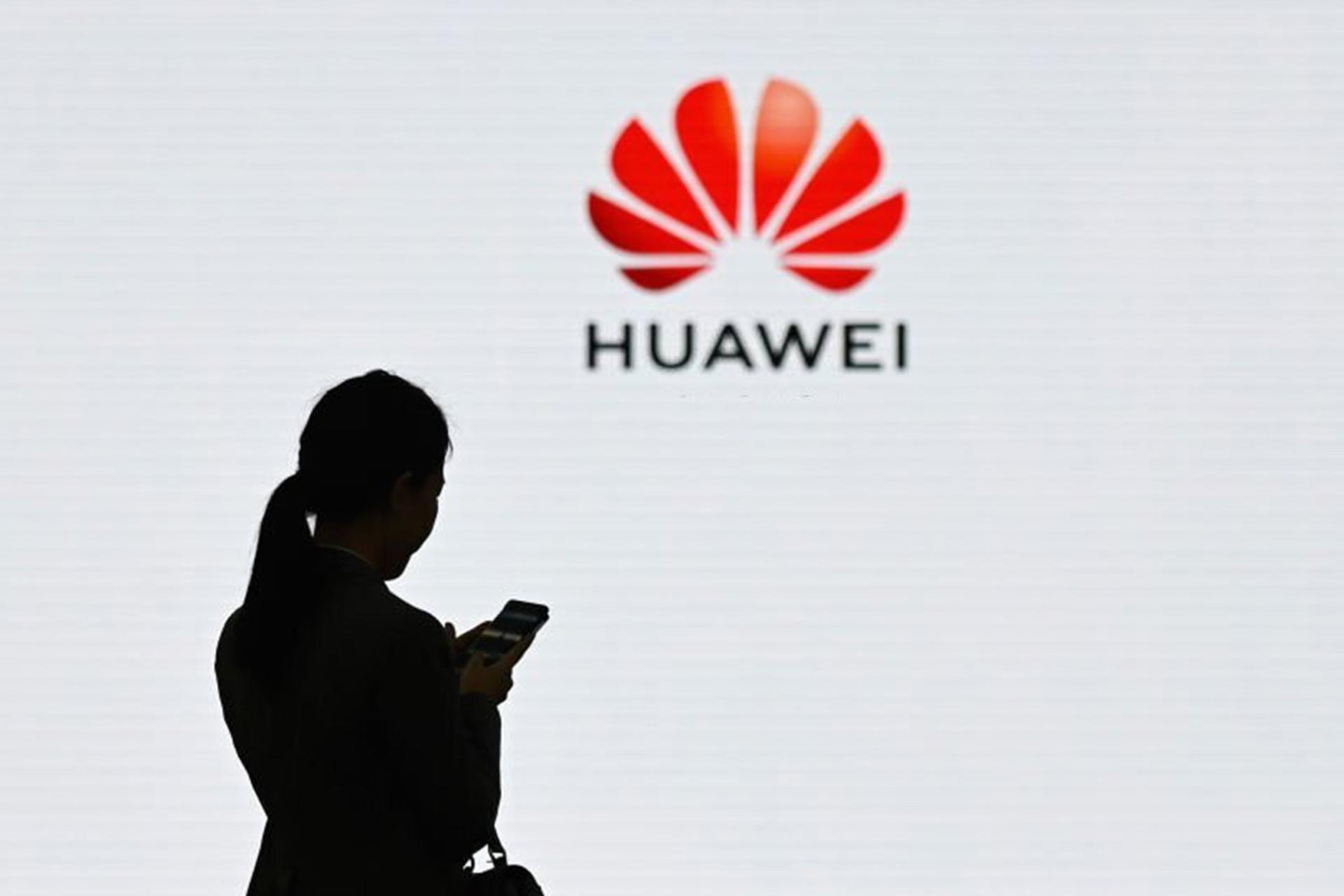 یک زن در حال استفاده از گوشی در برابر لوگو هواوی Huawei