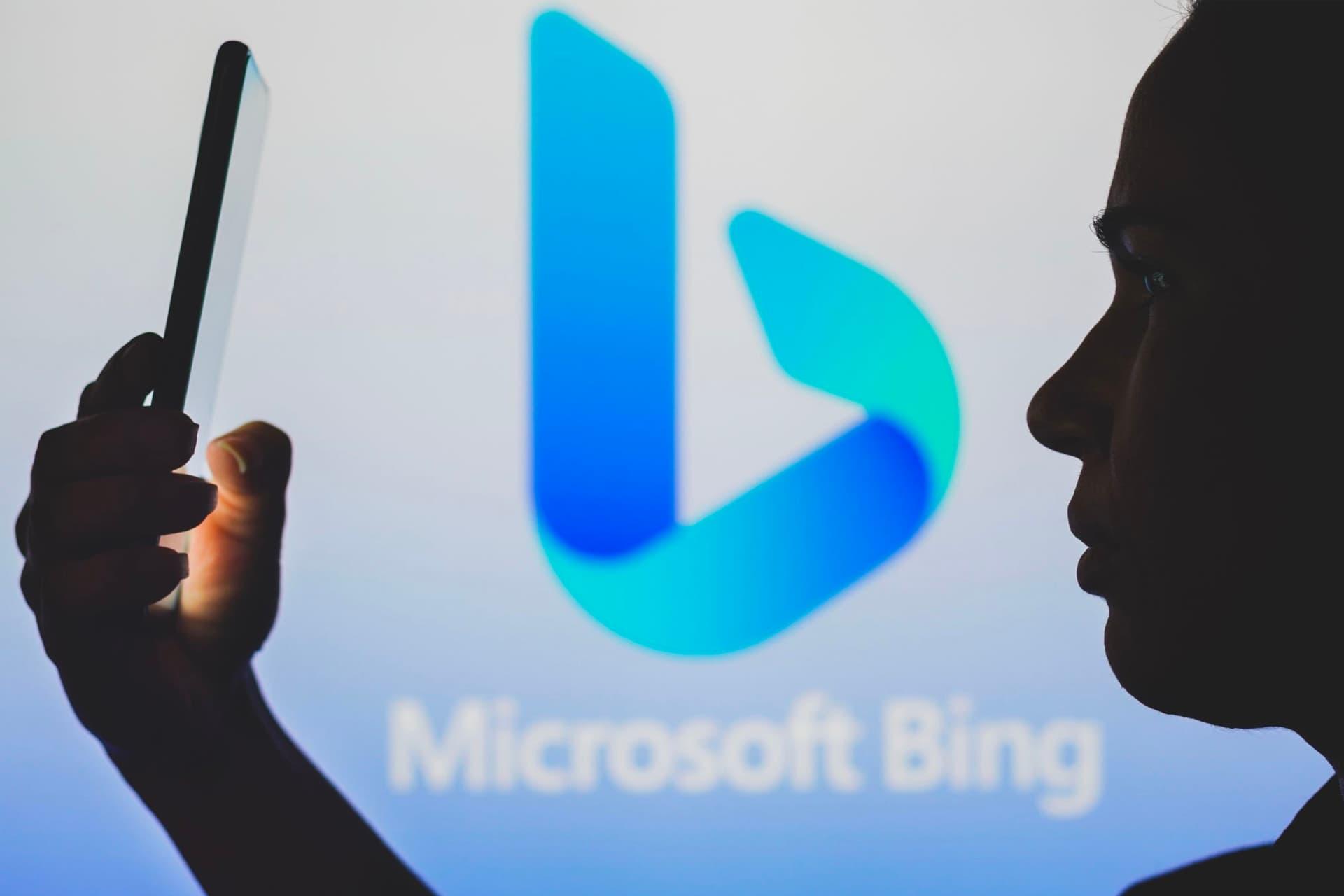 یک زن با گوشی موبایل در جلوی لوگو مایکروسافت بینگ / Microsoft Bing