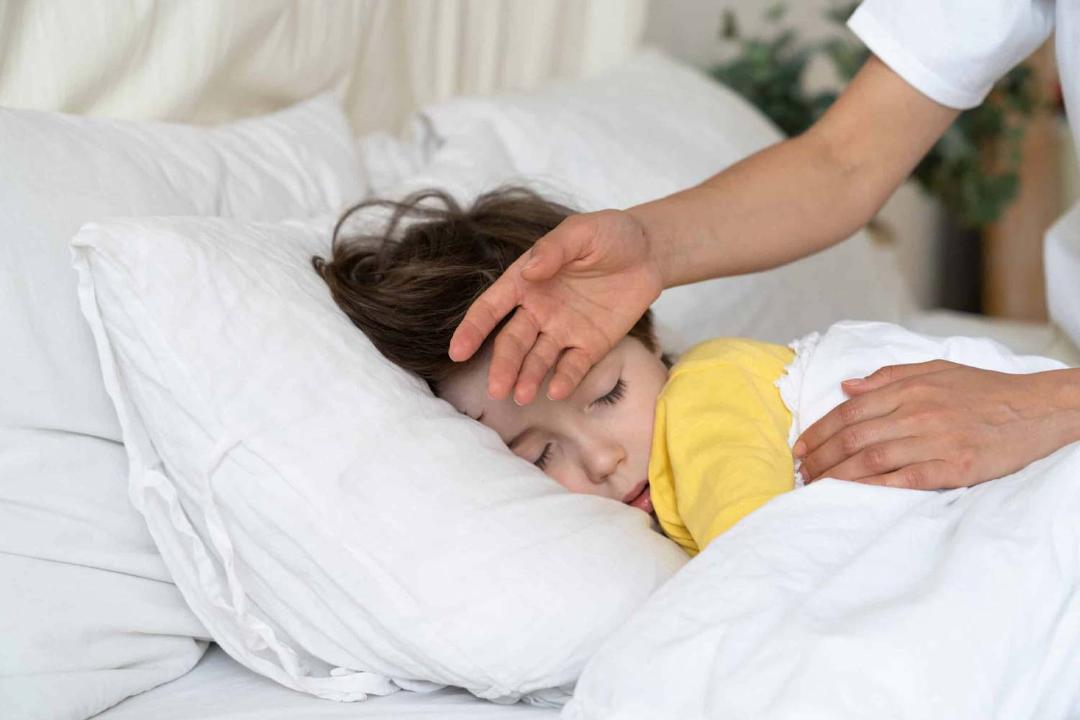 مادری در حال چک کردن دمای پسربچه‌ی خوابیده در تخت با پشت دست