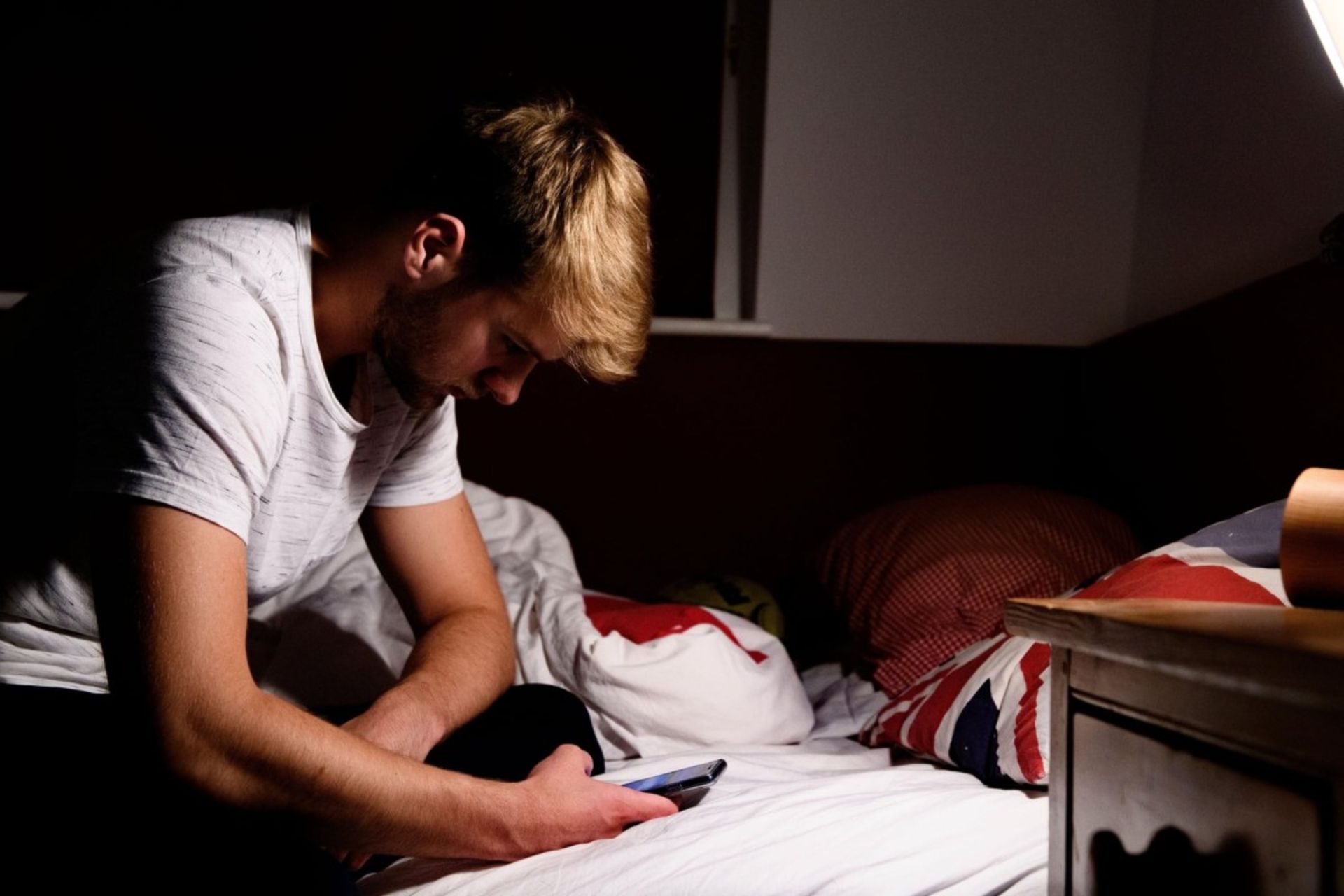 پسر جوان نشسته روی تخت در حال استفاده از گوشی